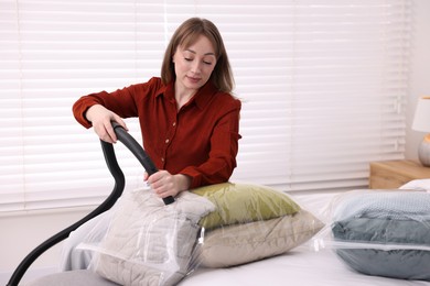 Woman sealing vacuum bag with pillows on bed at home