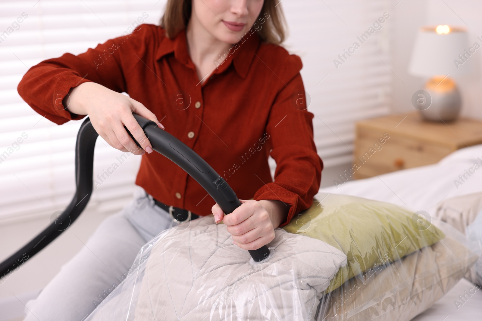 Photo of Woman sealing vacuum bag with pillows on bed at home, closeup