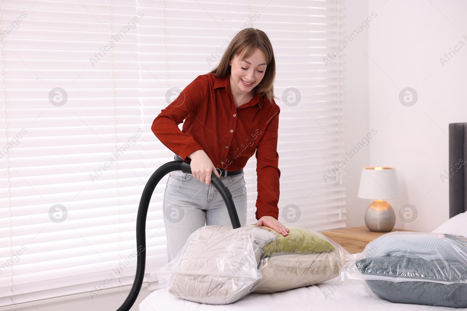 Photo of Woman sealing vacuum bag with pillows at home