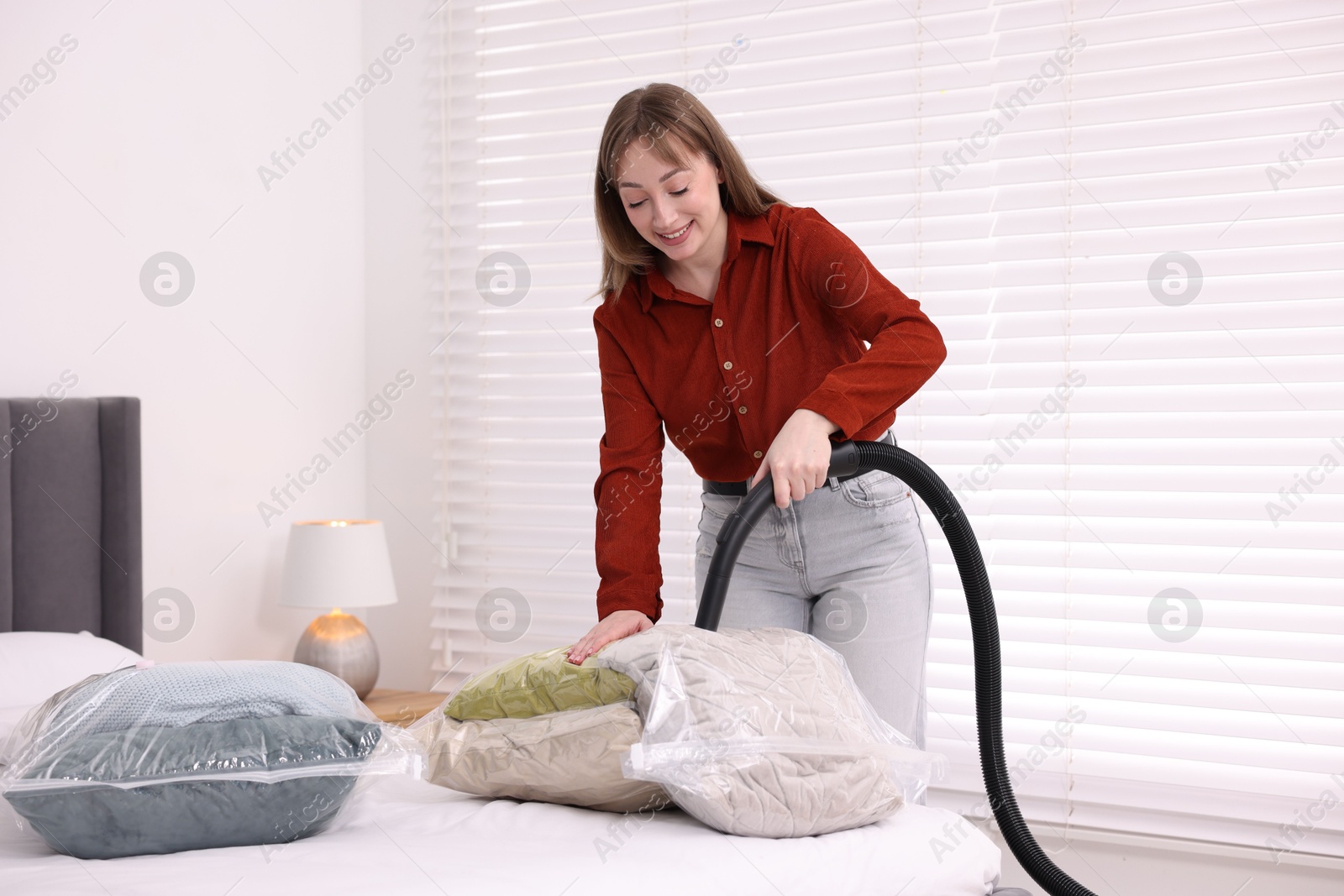 Photo of Woman sealing vacuum bag with pillows at home