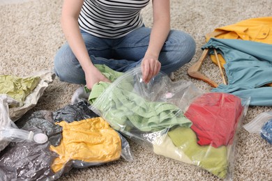 Photo of Woman packing clothes into vacuum bag on floor at home, closeup