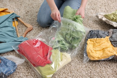 Photo of Woman packing clothes into vacuum bag on floor at home, closeup