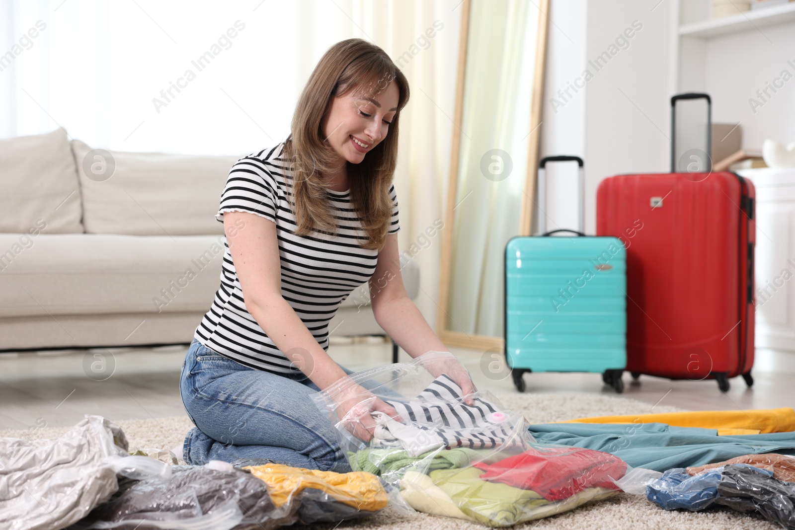 Photo of Woman packing clothes into vacuum bag on floor at home