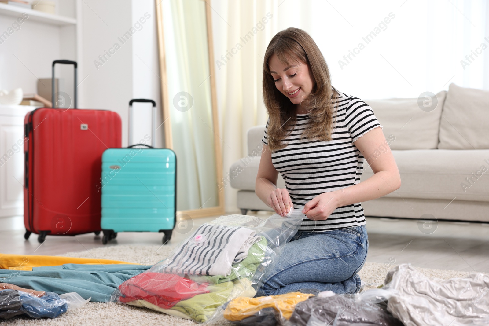 Photo of Woman packing clothes into vacuum bag on floor at home