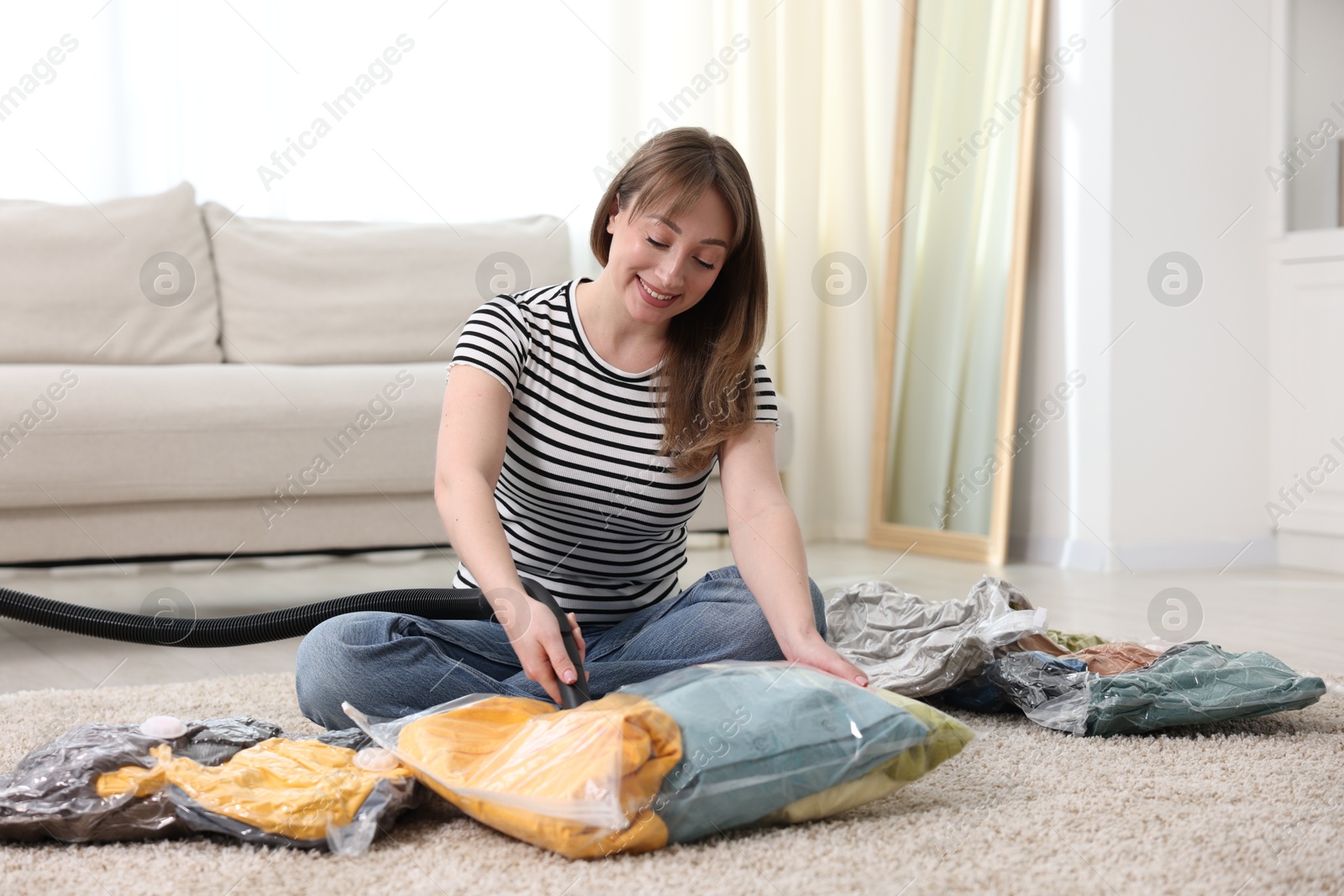 Photo of Woman sealing vacuum bag with clothes on floor at home