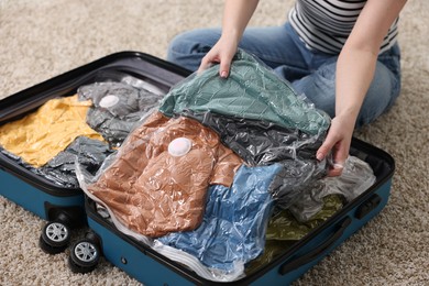 Photo of Woman packing clothes into vacuum bag on floor at home, closeup