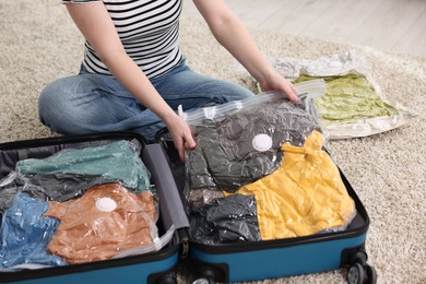 Photo of Woman packing clothes into vacuum bag on floor at home, closeup