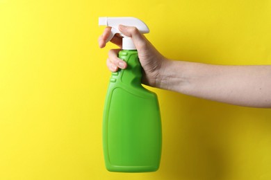 Photo of Woman with spray bottle of cleaning product on yellow background, closeup