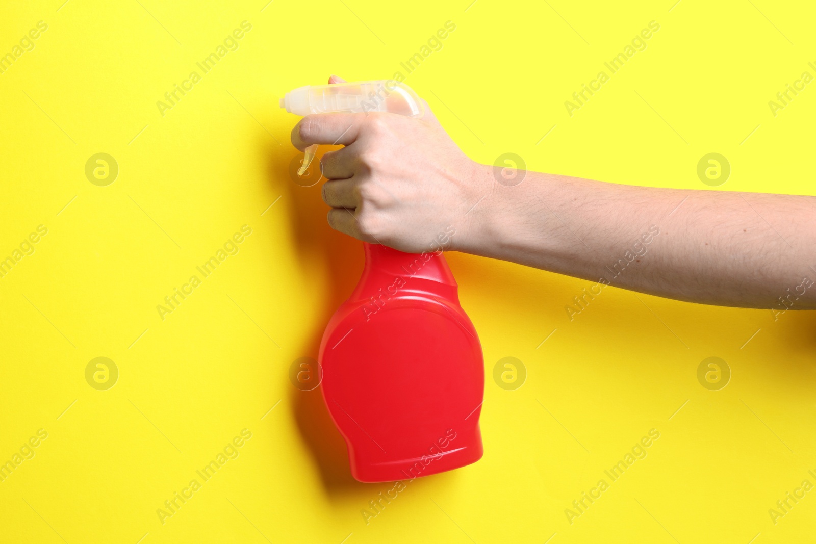 Photo of Woman with spray bottle of cleaning product on yellow background, closeup