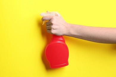 Photo of Woman with spray bottle of cleaning product on yellow background, closeup