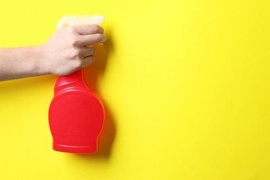 Photo of Woman with spray bottle of cleaning product on yellow background, closeup. Space for text