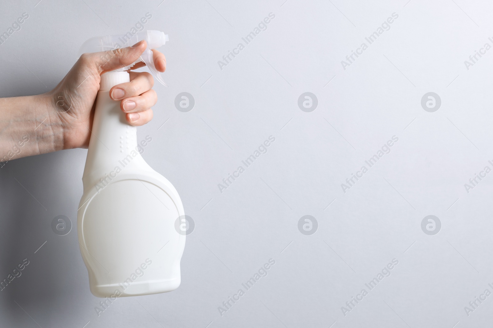 Photo of Woman with spray bottle of cleaning product on light grey background, closeup. Space for text