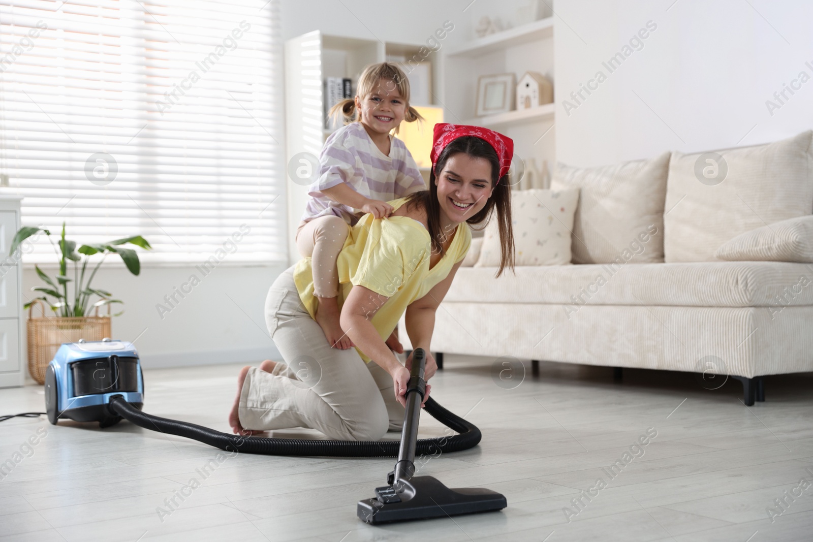 Photo of Little helper. Daughter and mother vacuuming together at home