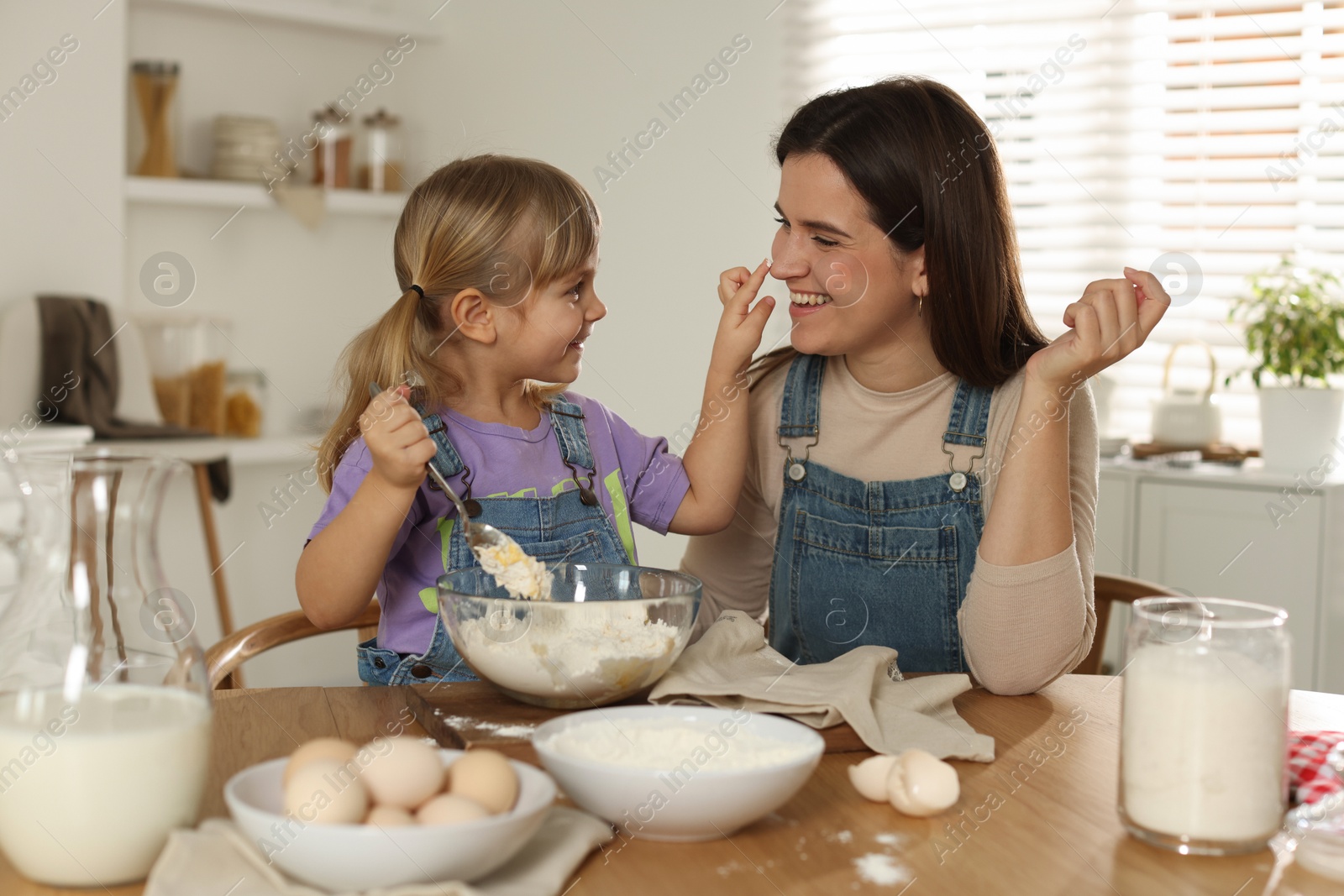 Photo of Little girl helping her mom making dough at table in kitchen