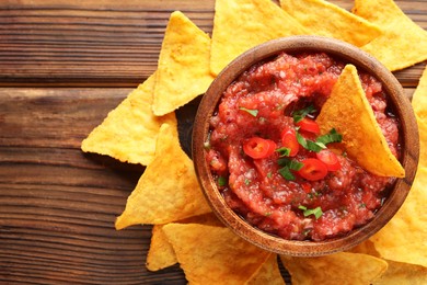 Photo of Delicious spicy salsa sauce in bowl and nacho chips on wooden table, flat lay. Space for text