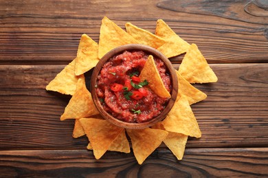 Photo of Delicious spicy salsa sauce in bowl and nacho chips on wooden table, flat lay