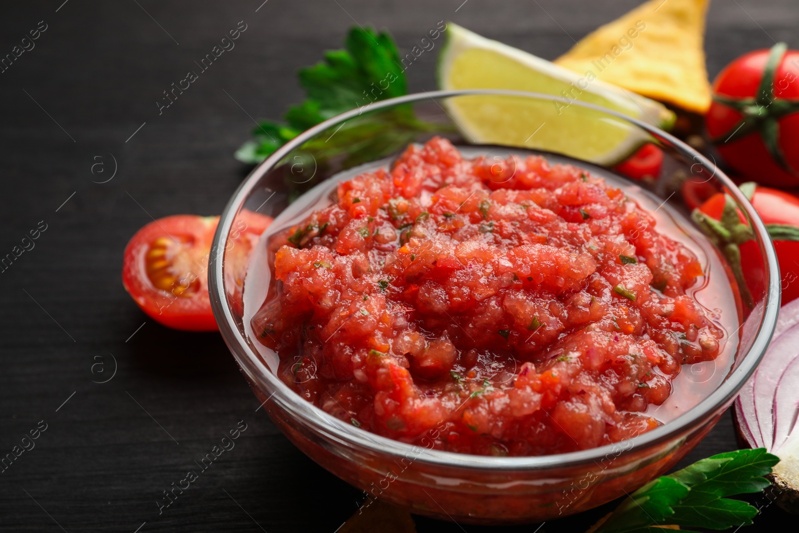 Photo of Spicy salsa sauce in bowl and ingredients on wooden table, closeup