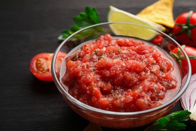 Photo of Spicy salsa sauce in bowl and ingredients on wooden table, closeup