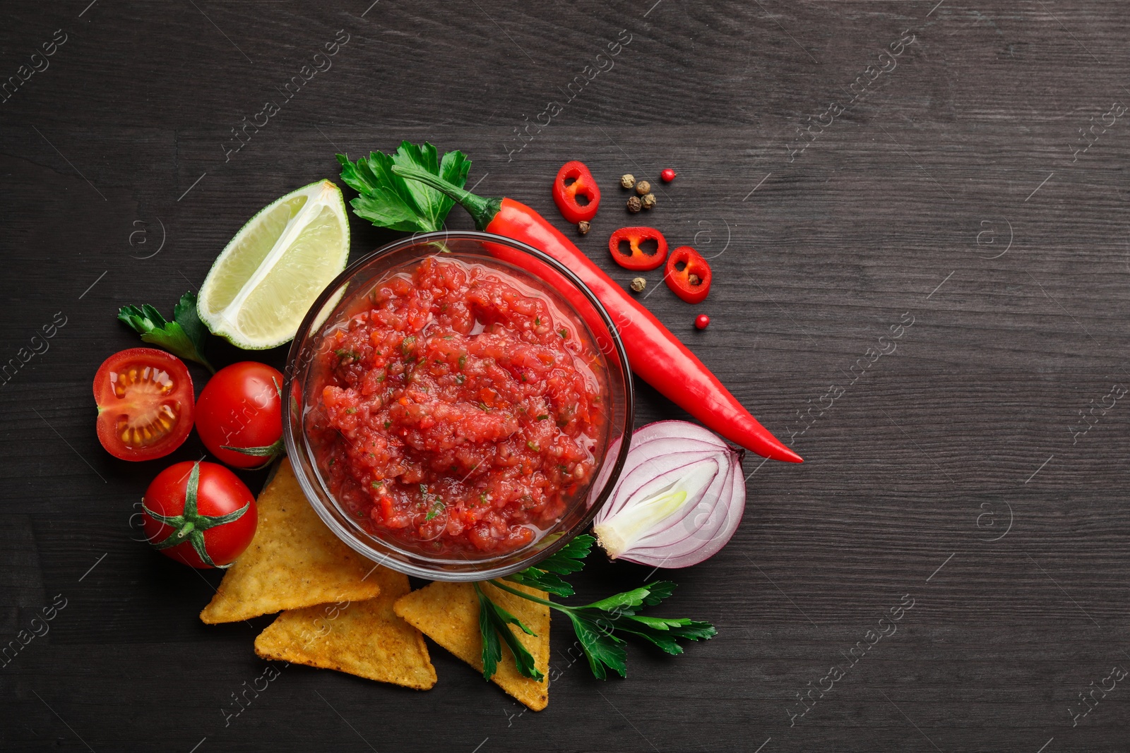 Photo of Spicy salsa sauce in bowl, nachos and ingredients on wooden table, flat lay. Space for text