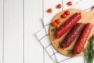 Photo of Different smoked sausages, cherry tomatoes and spices on white wooden table, flat lay. Space for text