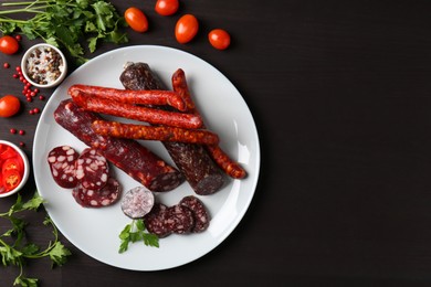 Photo of Different smoked sausages, cherry tomatoes and spices on dark wooden table, flat lay. Space for text