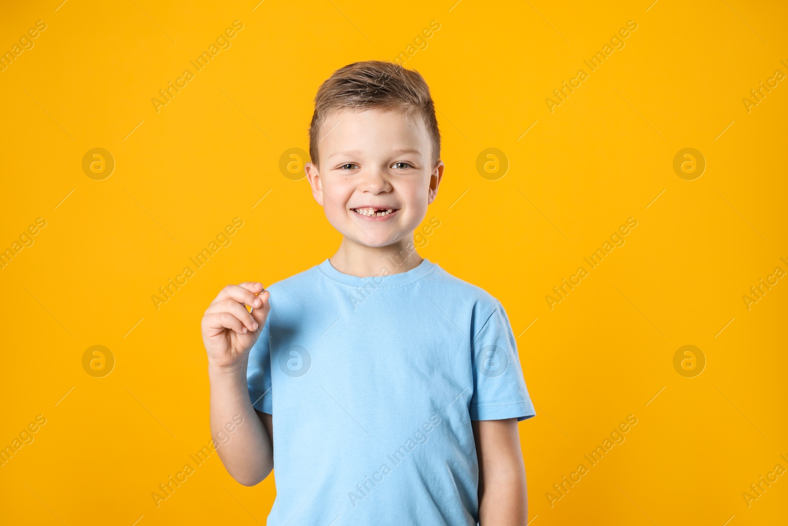 Photo of Cute little boy with missing tooth on orange background. Waiting for tooth fairy