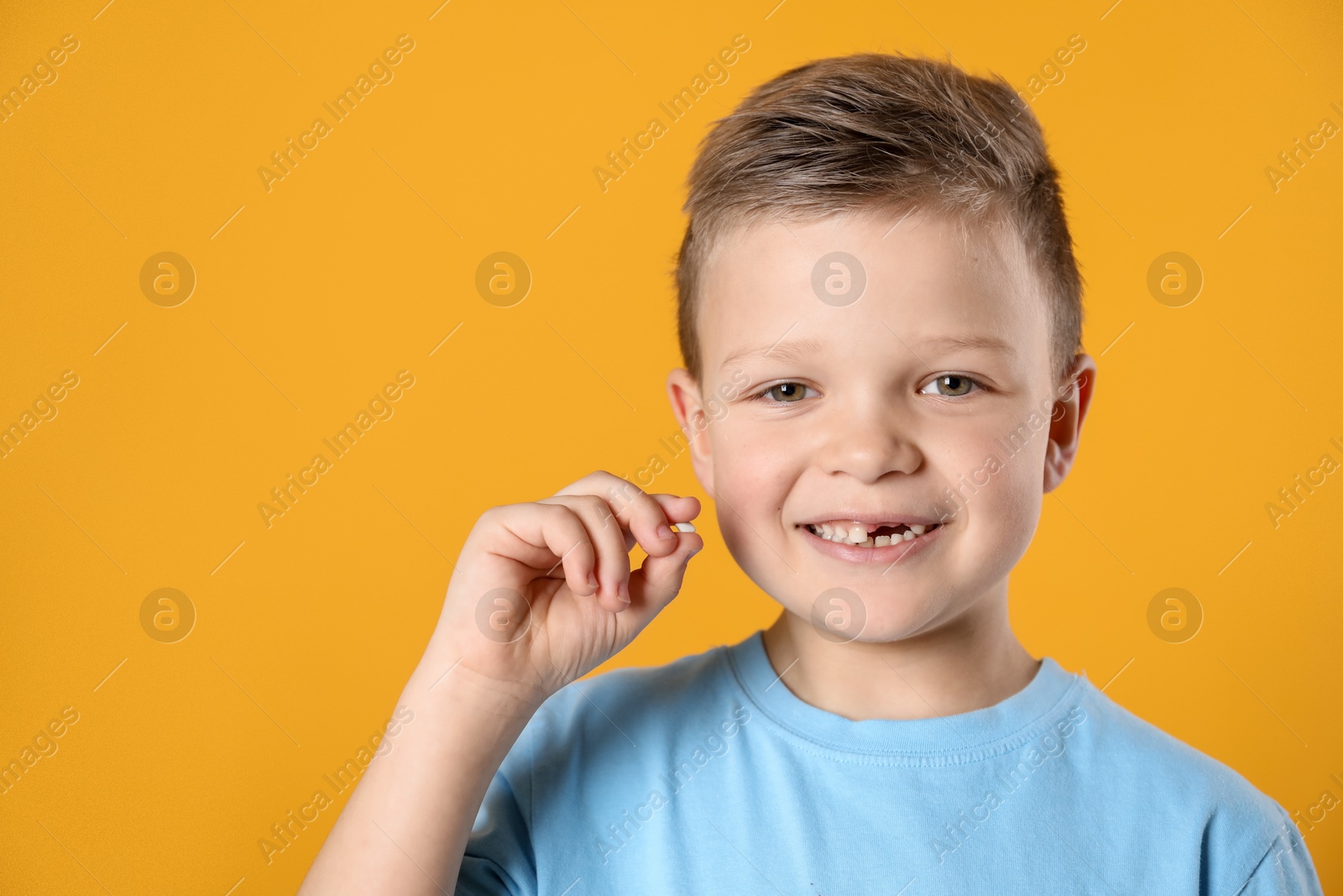 Photo of Cute little boy with missing tooth on orange background, space for text. Waiting for tooth fairy