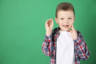 Cute little boy with missing tooth on green background, space for text. Waiting for tooth fairy