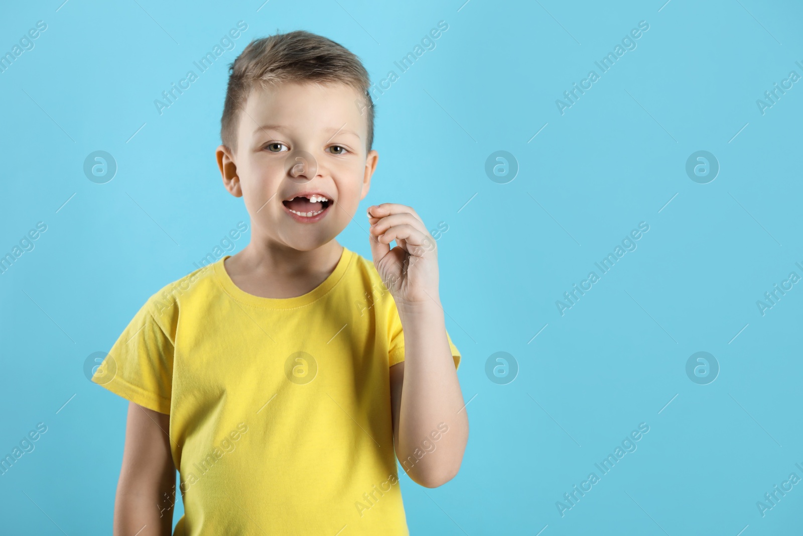 Photo of Cute little boy with missing tooth on light blue background, space for text. Waiting for tooth fairy