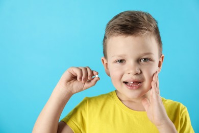 Photo of Cute little boy with missing tooth on light blue background. Waiting for tooth fairy