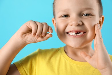 Photo of Cute little boy with missing tooth on light blue background, closeup. Waiting for tooth fairy