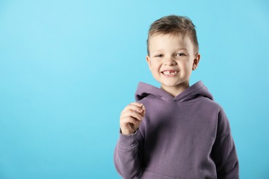 Photo of Cute little boy with missing tooth on light blue background, space for text. Waiting for tooth fairy