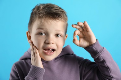 Photo of Cute little boy with missing tooth on light blue background. Waiting for tooth fairy