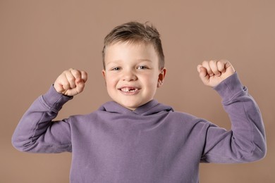 Photo of Cute little boy with missing tooth on dark beige background