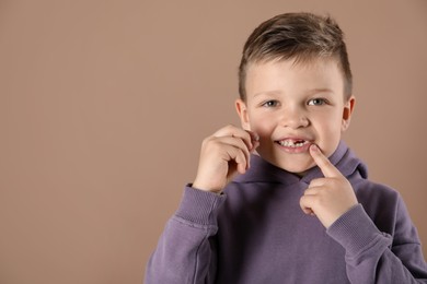 Cute little boy with missing tooth on dark beige background, space for text. Waiting for tooth fairy