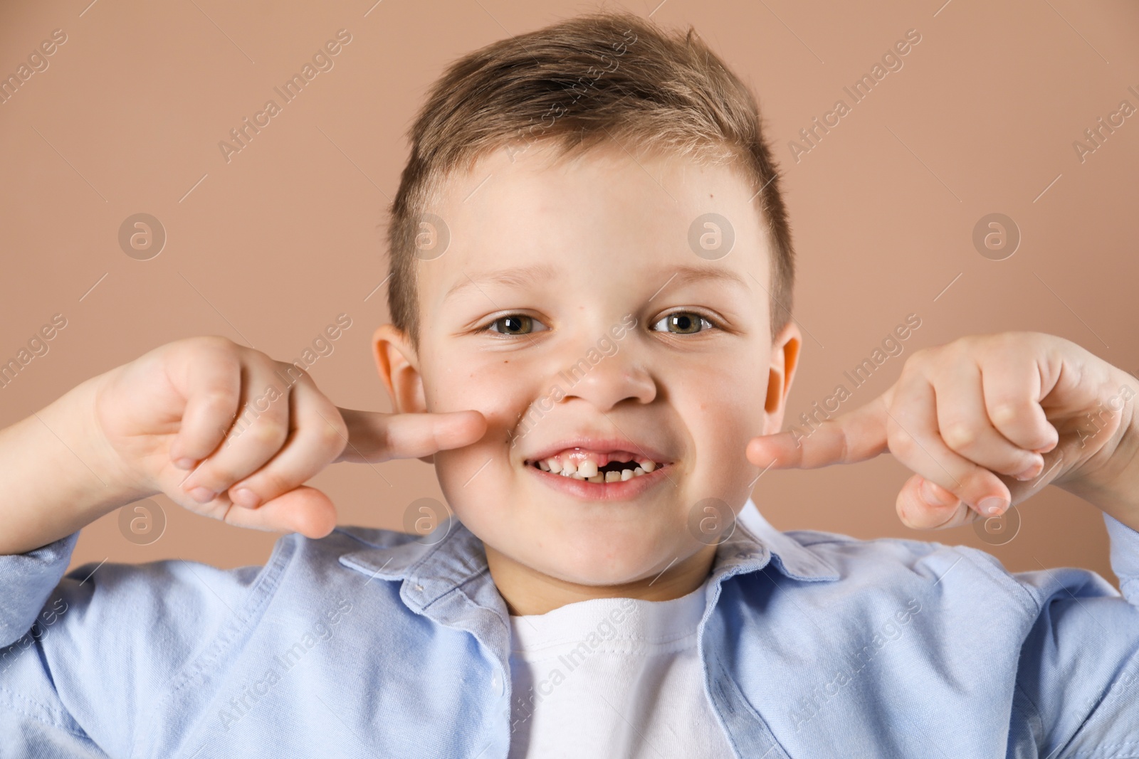 Photo of Cute little boy pointing at his missing tooth on dark beige background