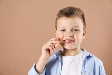 Photo of Cute little boy with missing tooth on dark beige background, space for text. Waiting for tooth fairy