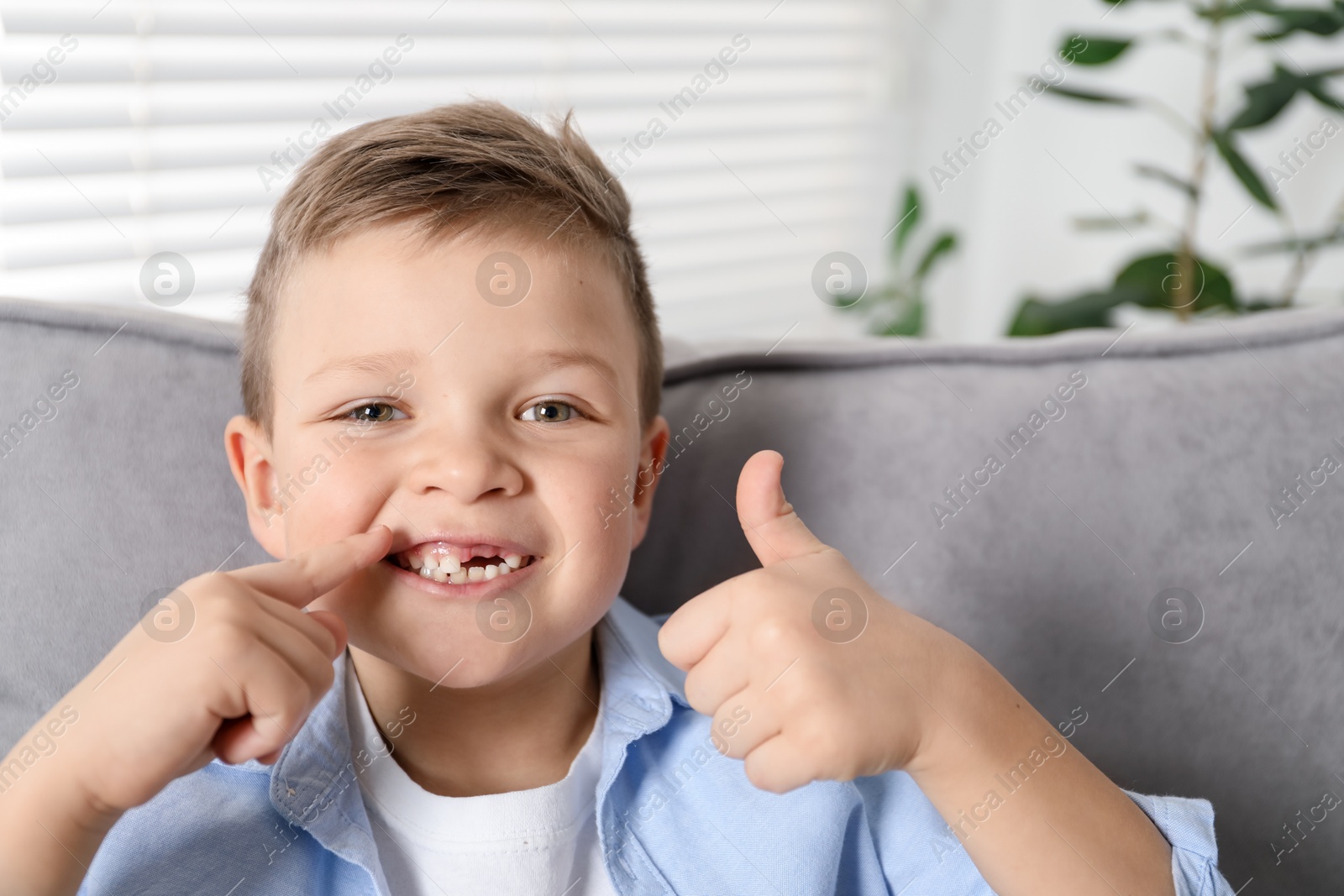 Photo of Cute little boy pointing at his missing tooth and showing thumbs up indoors