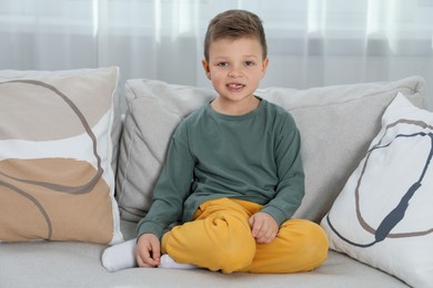 Cute little boy with missing tooth on sofa at home