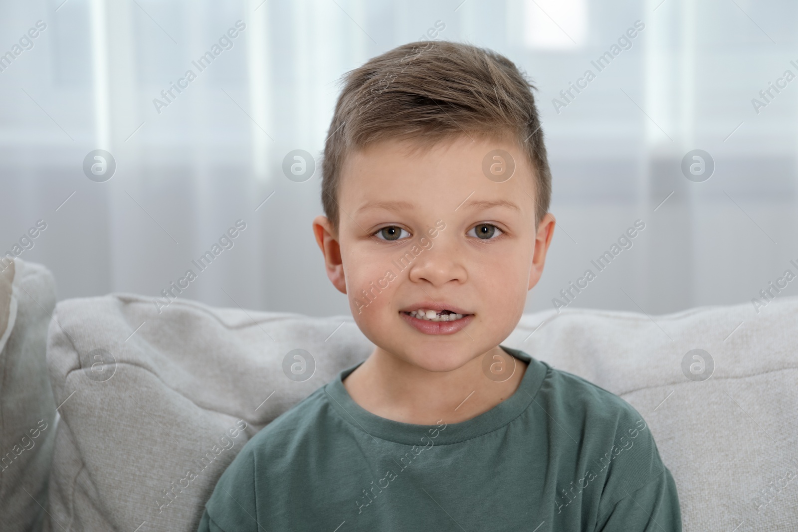 Photo of Cute little boy with missing tooth on sofa at home