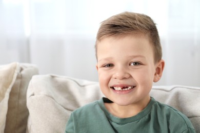 Photo of Cute little boy with missing tooth on sofa at home