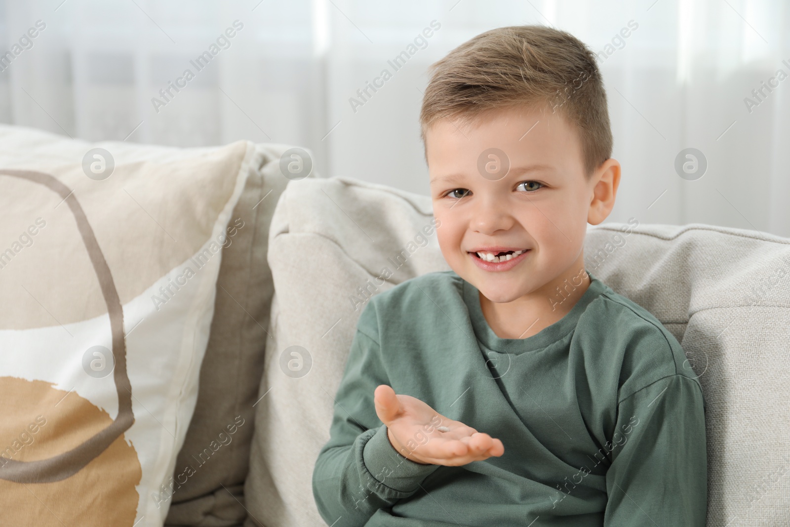 Photo of Cute little boy with missing tooth on sofa at home. Waiting for tooth fairy