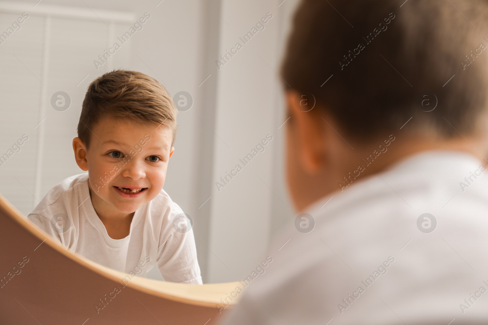 Photo of Cute little boy with missing tooth near mirror indoors