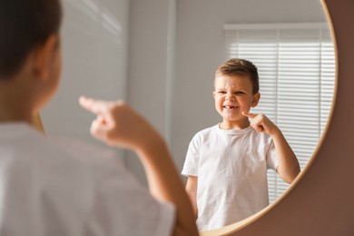 Photo of Cute little boy pointing at his missing tooth near mirror indoors