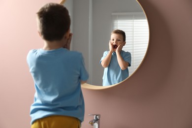 Photo of Cute little boy with missing tooth near mirror indoors