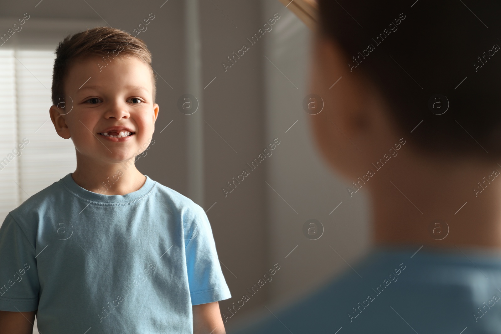 Photo of Cute little boy with missing tooth near mirror indoors