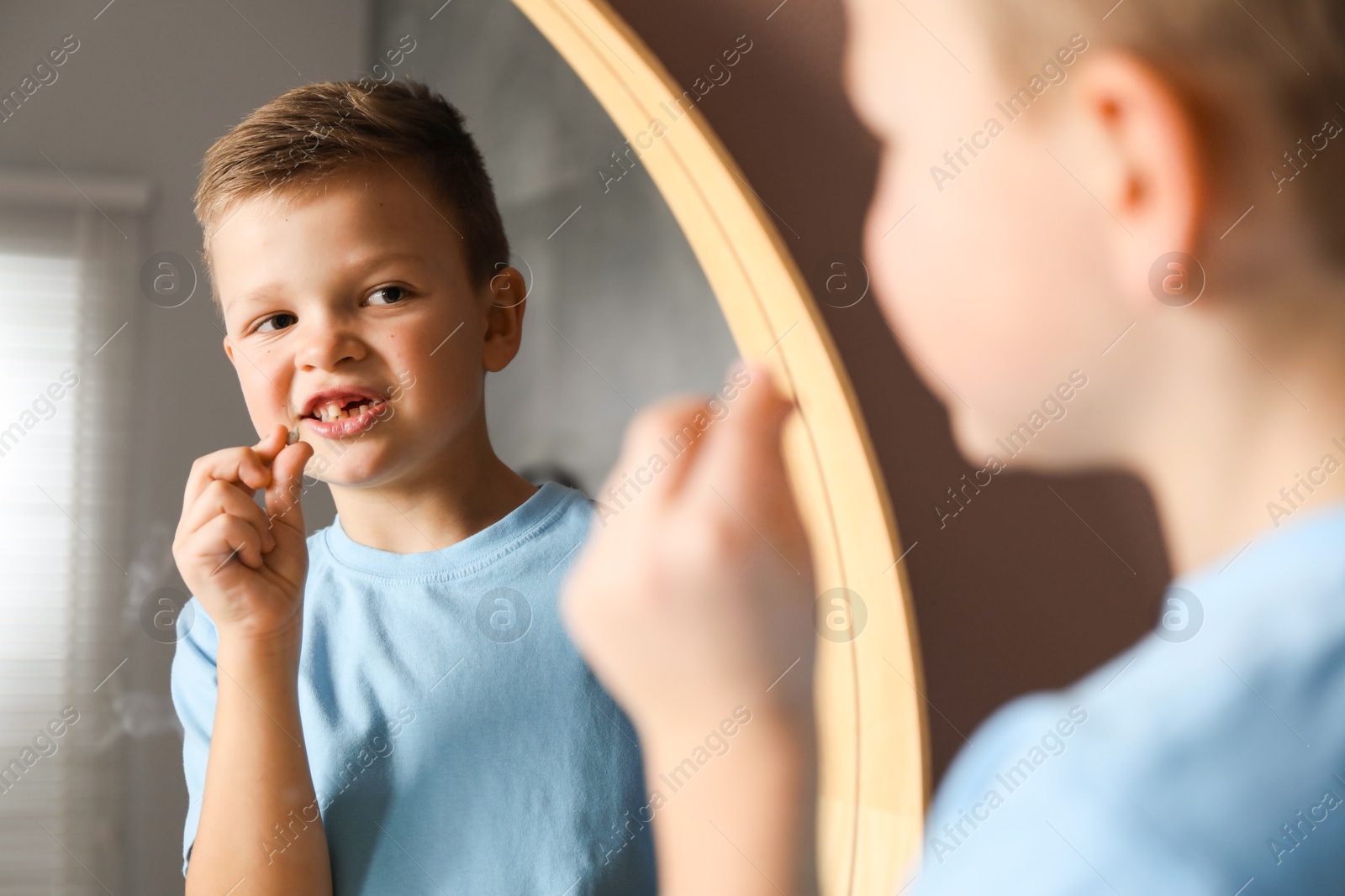 Photo of Cute little boy with missing tooth near mirror indoors. Waiting for tooth fairy