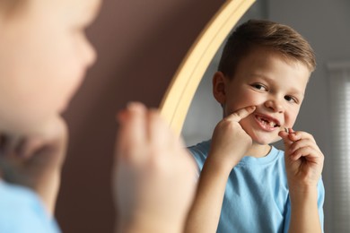 Photo of Cute little boy with missing tooth near mirror indoors. Waiting for tooth fairy