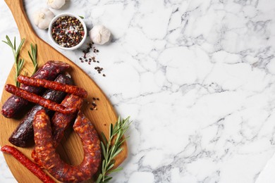 Photo of Different smoked sausages, rosemary and spices on white marble table, flat lay. Space for text