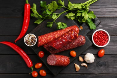 Photo of Different smoked sausages and products on black wooden table, flat lay